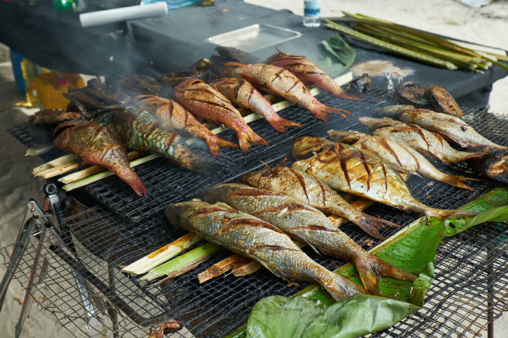 Ganze Fische brutzeln auf Bananenblättern über einem großen Grill.