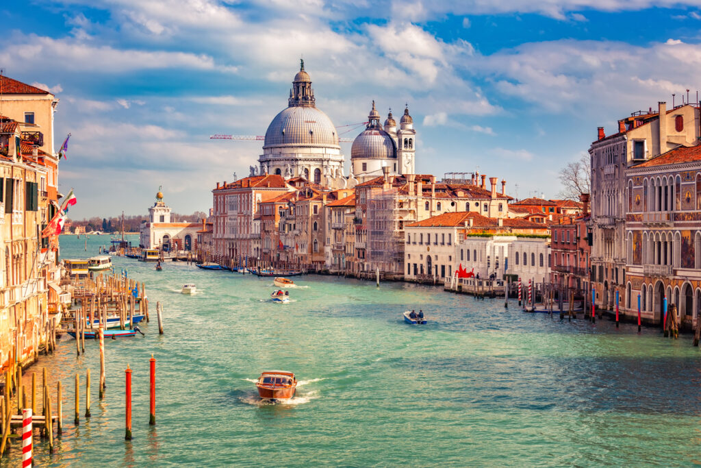 Blick entlang des Canal Grande in Venedig mit der barocken Basilika Santa Maria della Salute, historischen Palazzi und Booten auf türkisfarbenem Wasser.