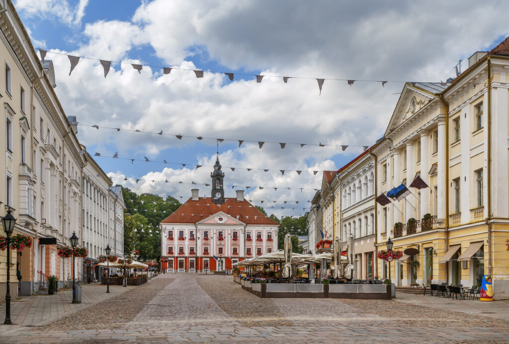 Der Raekoja plats zeigt das rote Rathaus umgeben von hellen Fassaden und Straßencafés.