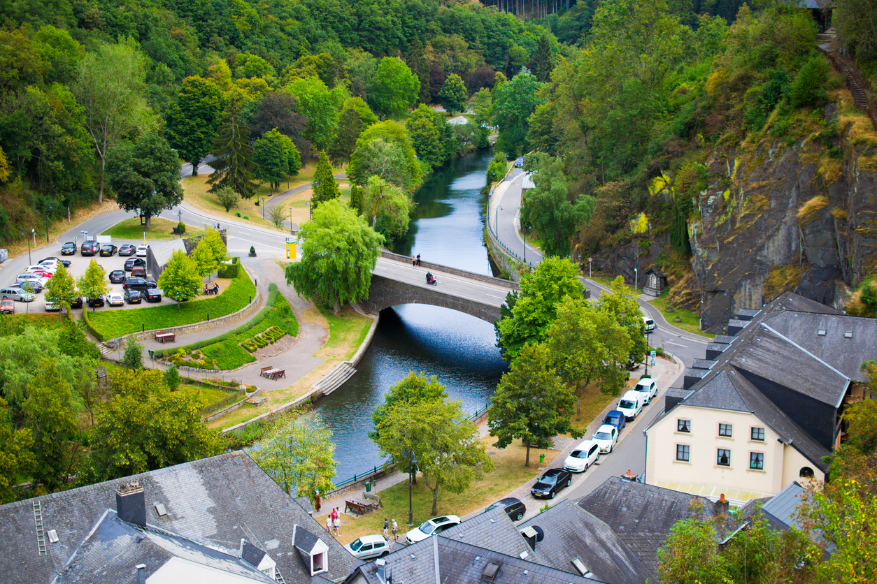 Luftaufnahme einer Brücke über die Sauer mit Parkplätzen, Grünflächen und umliegenden Häusern in Esch-sur-Sûre.