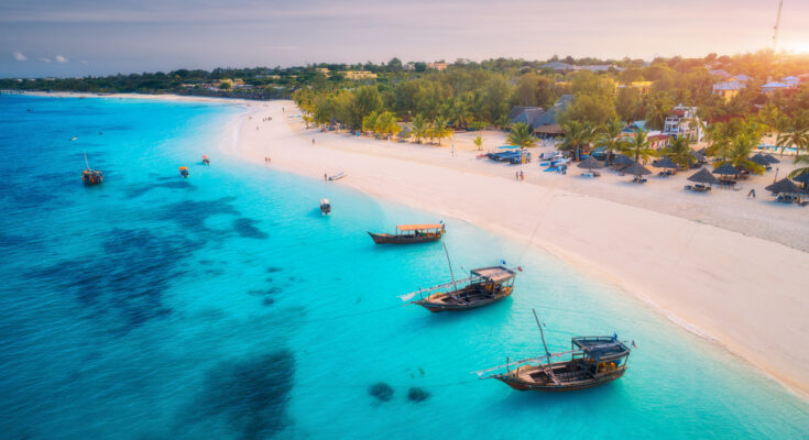 Breiter Sandstrand im Norden Sansibars mit Palmen, flachem türkisblauem Wasser und traditionellen Dhaus.