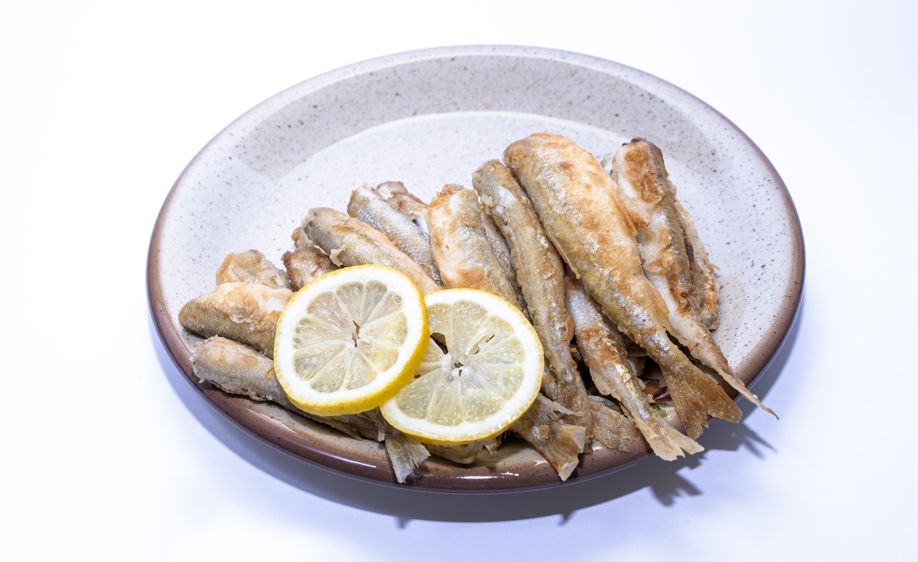 Teller mit goldbraun frittierten kleinen Fischen und zwei Zitronenscheiben.