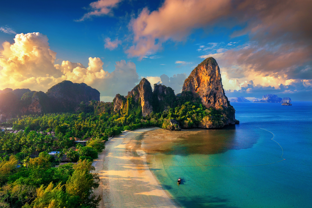 Weitwinkelaufnahme von Railay Beach mit steilen Kalksteinfelsen, langem Sandstrand und türkisfarbenem Meer unter dramatischen Wolken.
