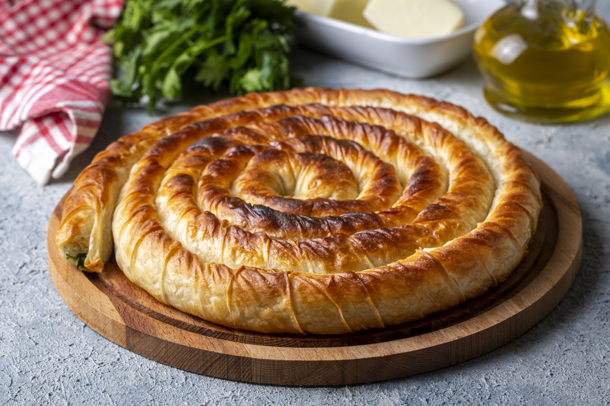 Spiral-Burek als Balkangericht, goldbraun gebacken auf einem Holzbrett.
