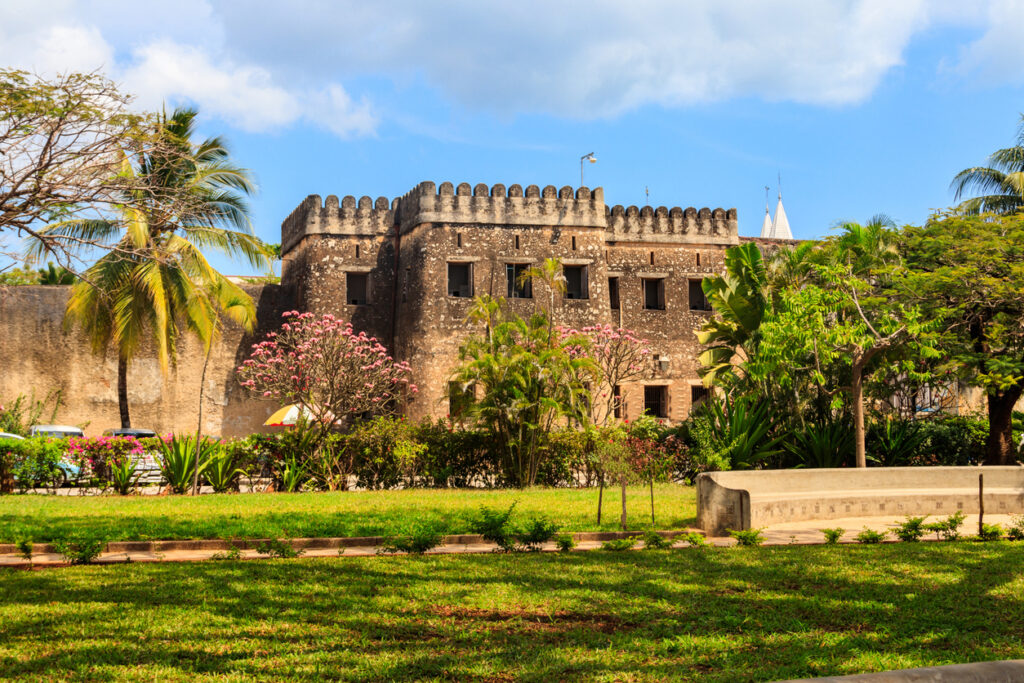 Historische Festung aus ockerfarbenem Stein in Stone Town, umgeben von Palmen und Garten.