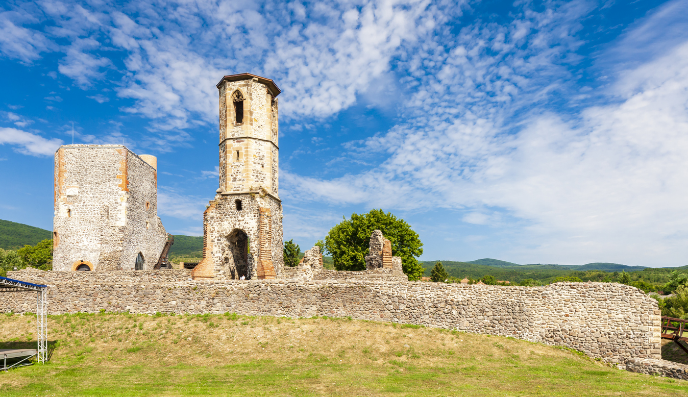 Steinmauern und Turm der Festung Eger vor hügeliger Landschaft.