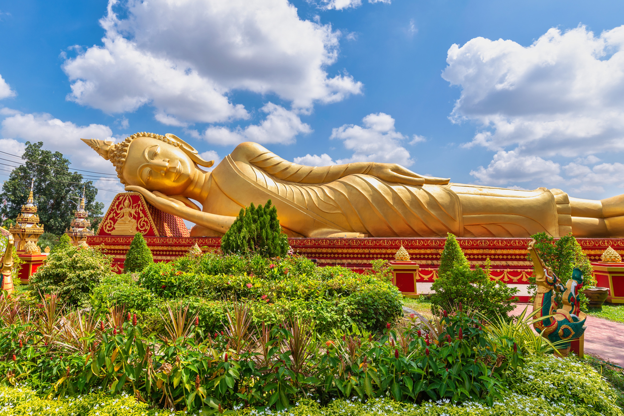 Große goldene Buddha-Statue in einem Tempelgarten unter blauem Himmel.