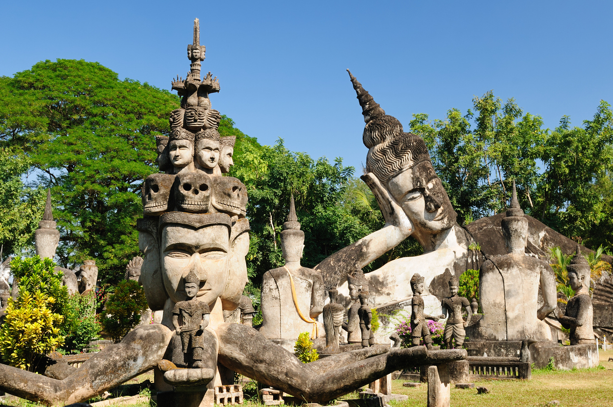 Betonfiguren und liegender Kopf zwischen Bäumen im Xieng-Khuan Park.