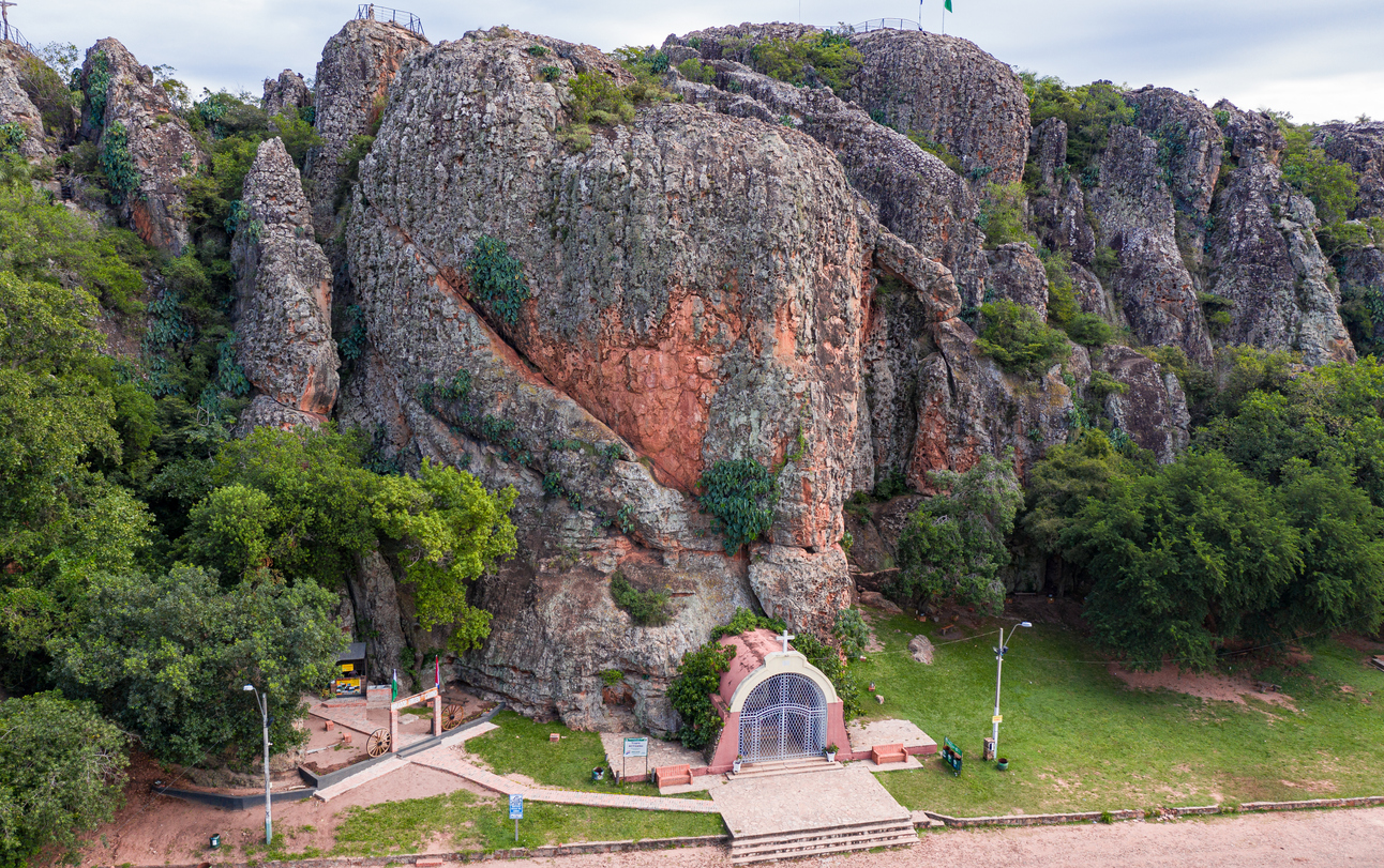 Kleine Felskapelle am Fuß einer riesigen, bewachsenen Klippe in Paraguay.