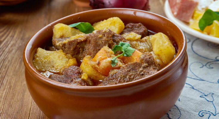 Brauner Keramiktopf mit finnischem Karjalanpaisti aus Fleisch, Kartoffeln und Möhren.
