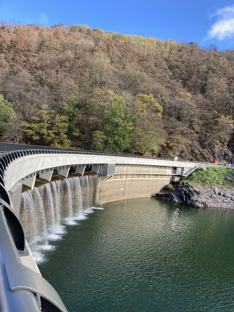 Blick auf die Staumauer mit herabstürzendem Wasser und herbstlich gefärbtem Wald bei Esch-sur-Sûre.