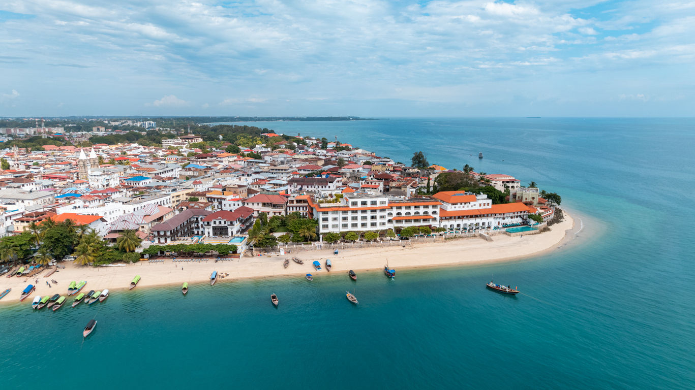 Luftaufnahme von Stone Town mit Strand, weißen Häusern und blauem Meer.