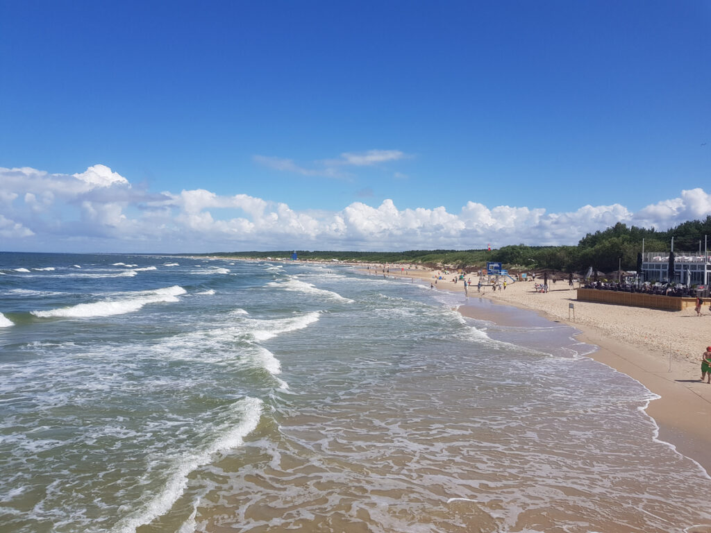 Weitläufiger Ostseestrand mit sanfter Brandung, Besuchern und blauem Himmel in Klaipėda.