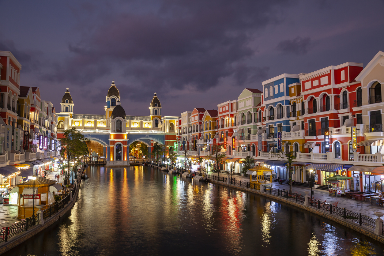 Bunte Fassaden und eine beleuchtete Brücke spiegeln sich im Kanal.