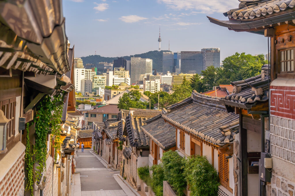 Traditionelle Hanok-Häuser in Bukchon mit Namsan Tower und Hochhäusern im Hintergrund.