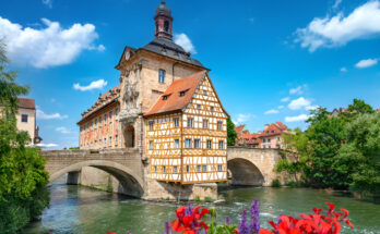 Fachwerk-Rathaus auf einer Brücke in Bamberg mit Blumen im Vordergrund.