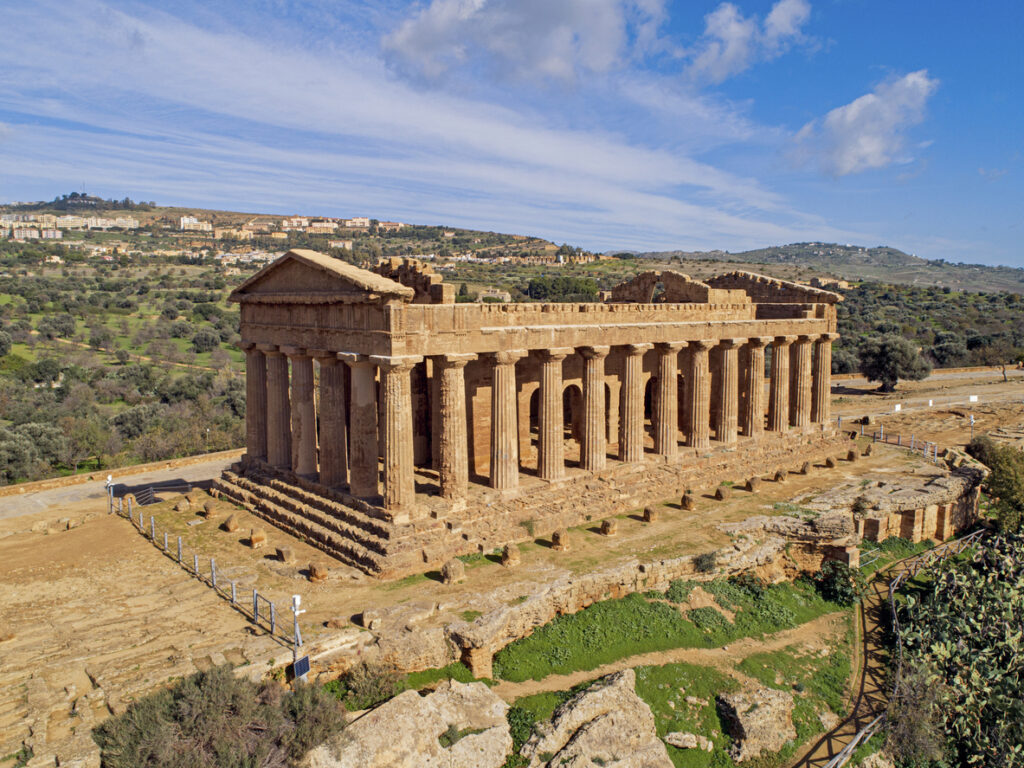 Tempel der Concordia im Tal der Tempel bei Agrigento auf Sizilien mit dorischen Säulen vor Hügelland und blauem Himmel.