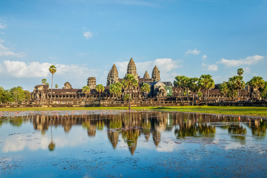 Der Tempel Angkor Wat spiegelt sich in einem Seerosenteich unter blauem Himmel.