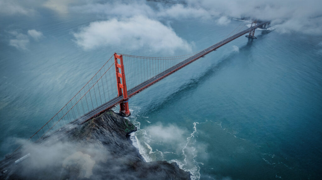 Luftaufnahme der roten Golden Gate Bridge über türkisblauem Wasser, teilweise vom Nebel umhüllt.