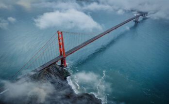 Luftaufnahme der roten Golden Gate Bridge über türkisblauem Wasser, teilweise vom Nebel umhüllt.