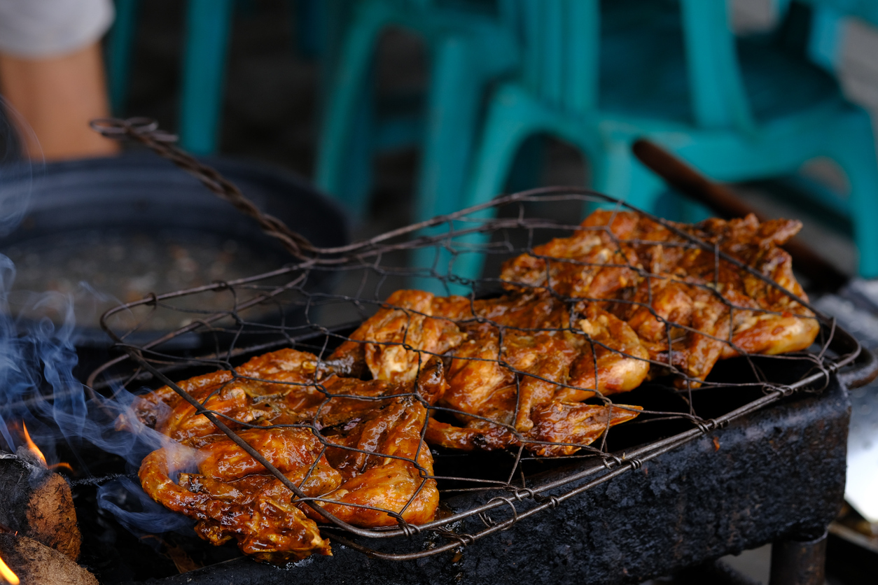Mariniertes Hähnchen wird auf einem Drahtrost über Holzkohle gegrillt.