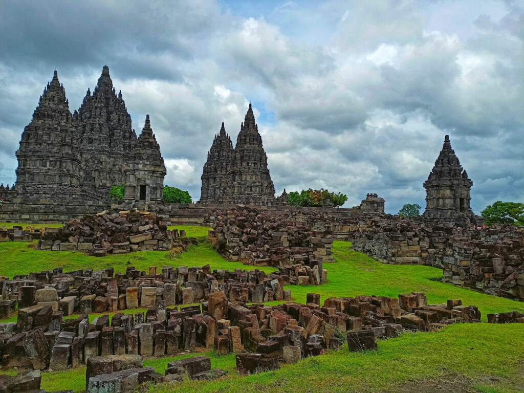 Hohe, filigrane Tempeltürme von Prambanan mit Trümmern im Vordergrund.