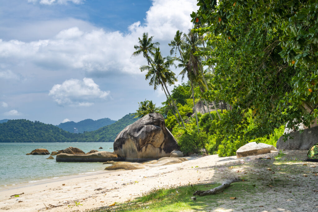 Sandstrand auf Penang mit Palmen, großen Felsblöcken und ruhiger Bucht.