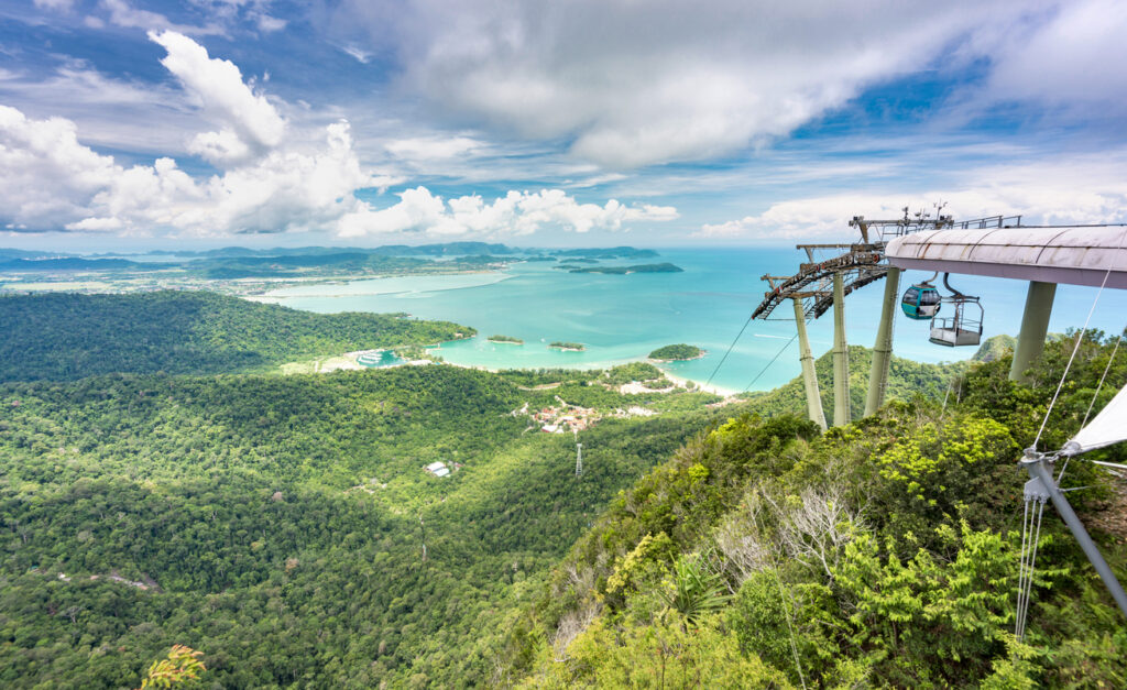 Gondeln der Langkawi-Seilbahn schweben über bewaldeten Hügeln mit Blick auf Buchten und kleine Inseln.