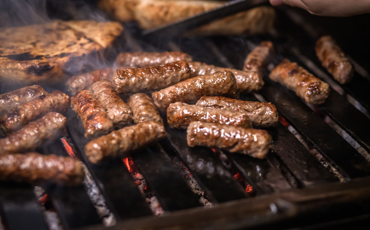 Rauchende Cevapčiči braten über glühenden Kohlen.