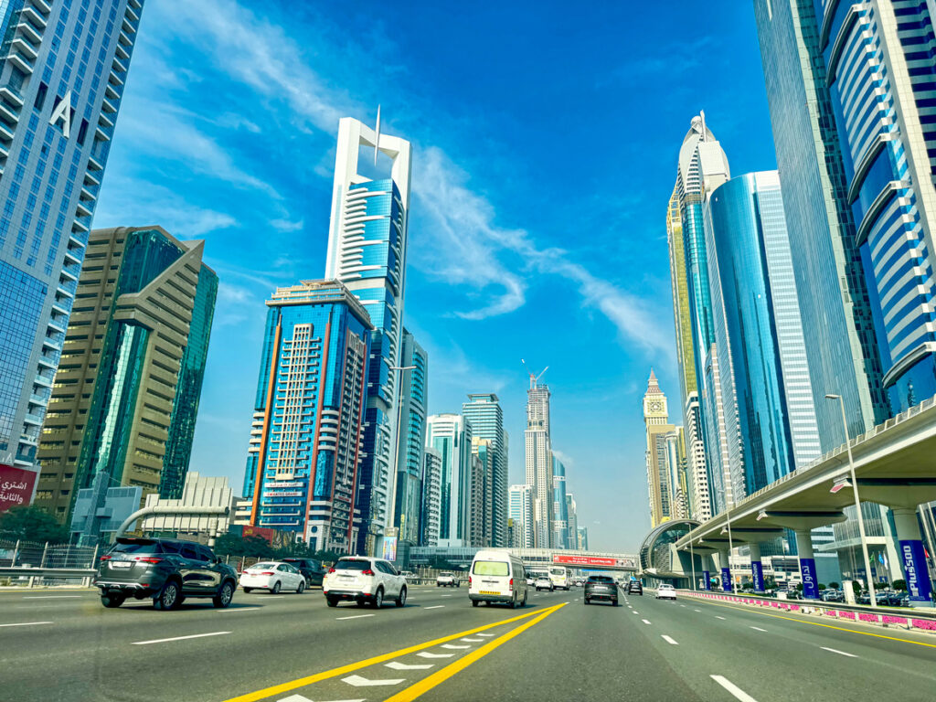 Mehrspurige Autobahn zwischen gläsernen Wolkenkratzern unter blauem Himmel.