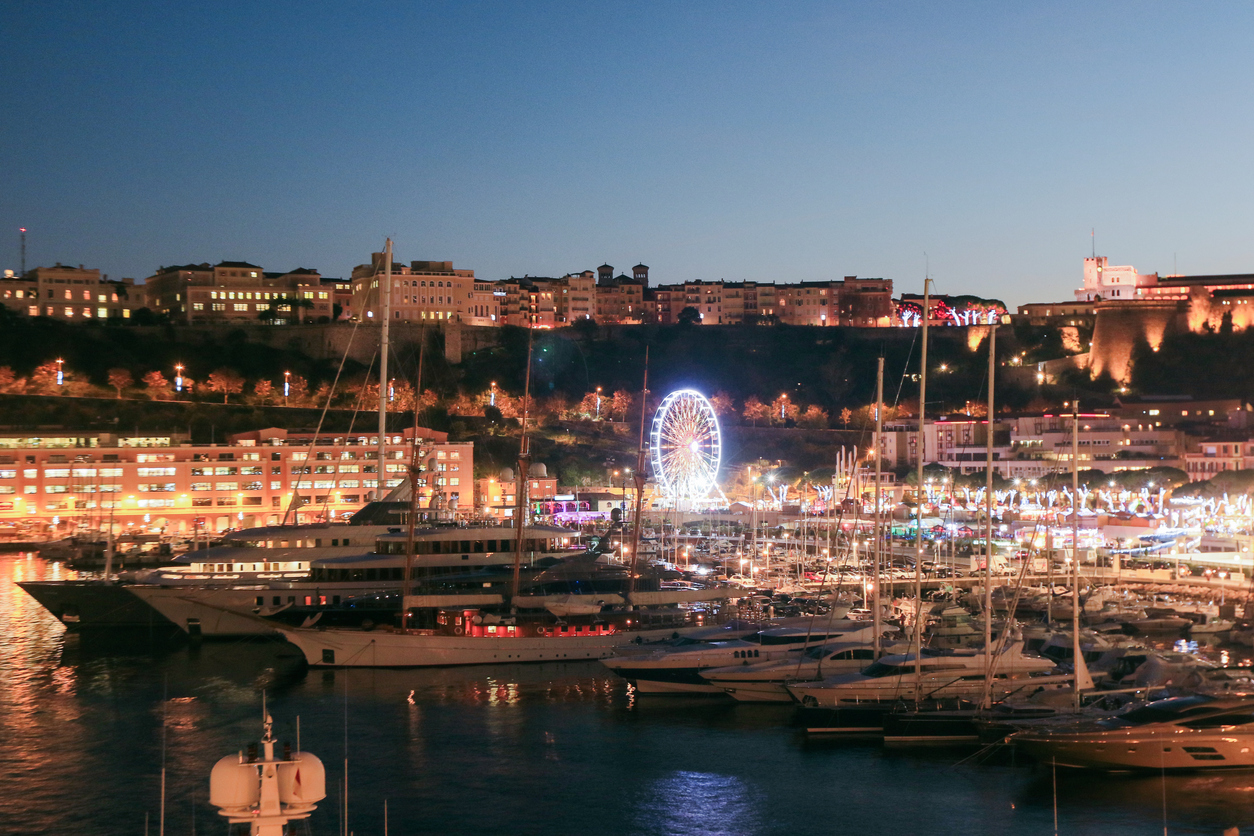 Yachthafen von Monaco im Abendlicht mit Riesenrad und beleuchteter Altstadt.