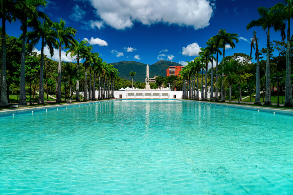 Ein langes türkisfarbenes Becken ist von Palmen und Bergen gerahmt.