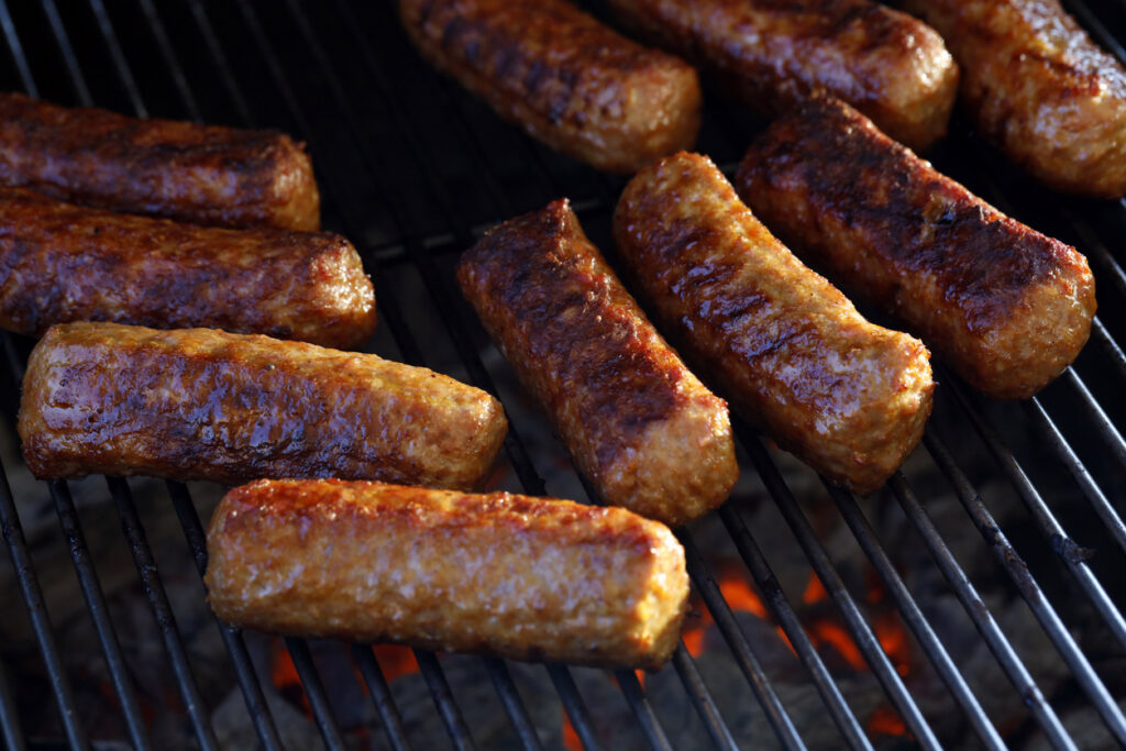 Mehrere Cevapcici liegen auf einem Grillrost über glühender Holzkohle.