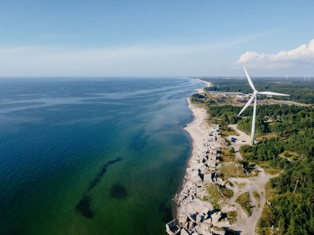 Luftaufnahme der Küste von Liepāja mit Windkraftanlage und Ruinen der Nordforts am Strand.
