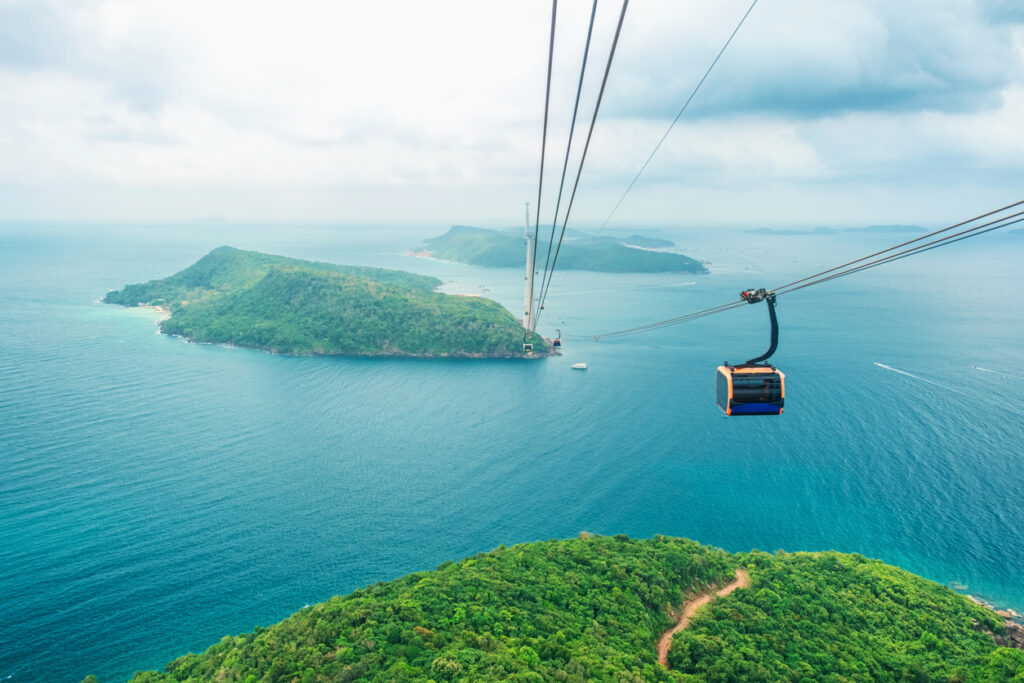Eine Gondel schwebt über türkisblauem Wasser und Inseln.
