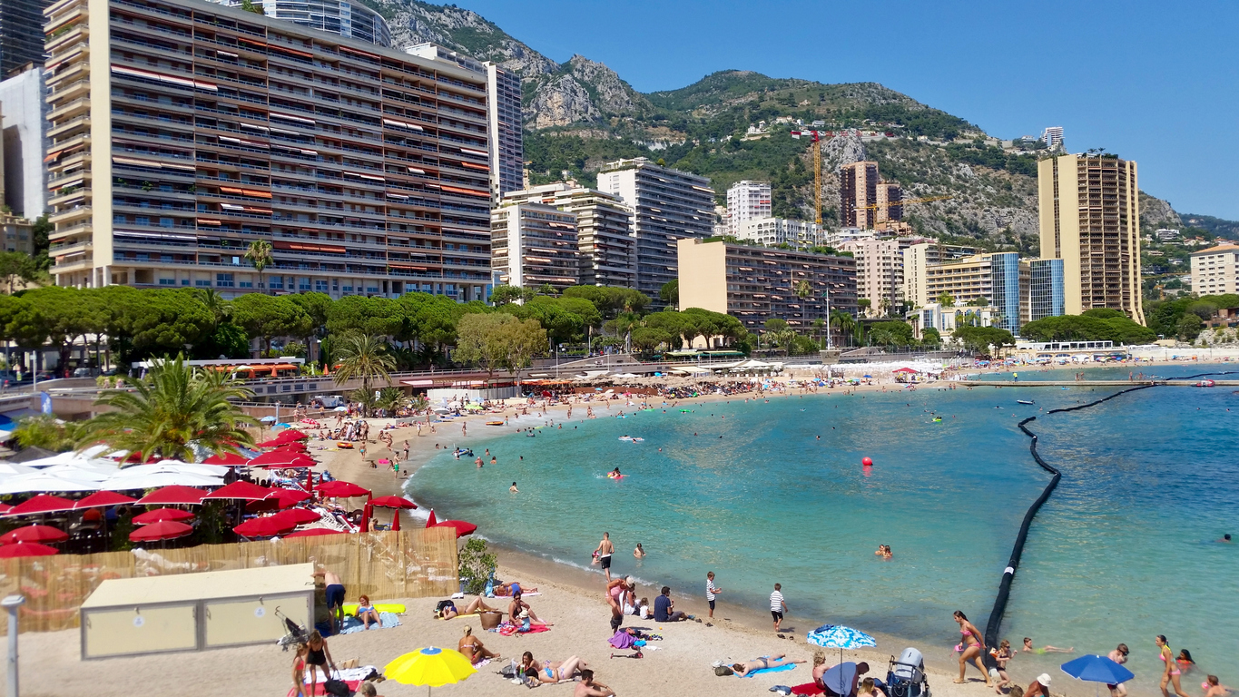 Feiner Stadtstrand von Monaco mit türkisblauem Wasser und Hochhäusern im Hintergrund.