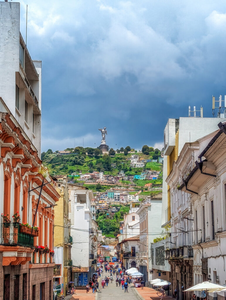 Fußgängerstraße mit Kolonialhäusern und Blick auf den Hügel mit Statue in Quito.