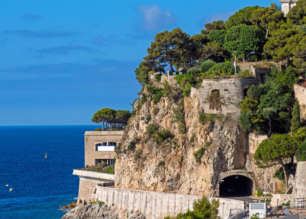 Steile Felsklippe mit Tunnel, Bäumen und Mittelmeer in Monaco.