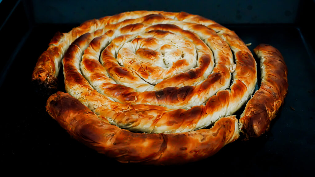 Spiralförmiger Burek mit knusprigem Teig auf dem Blech.