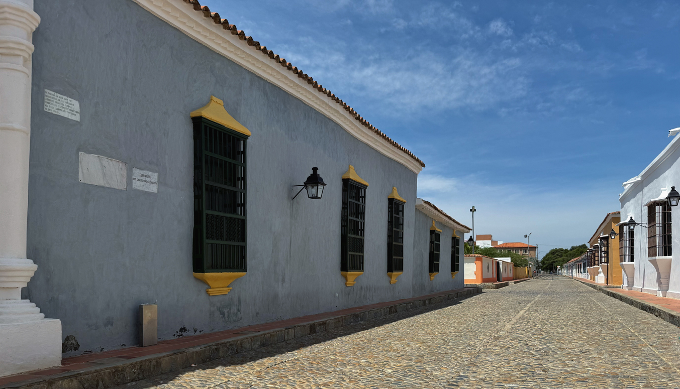 Gepflasterte Straße mit pastellfarbenen Kolonialhäusern und gelb gerahmten Fenstern.