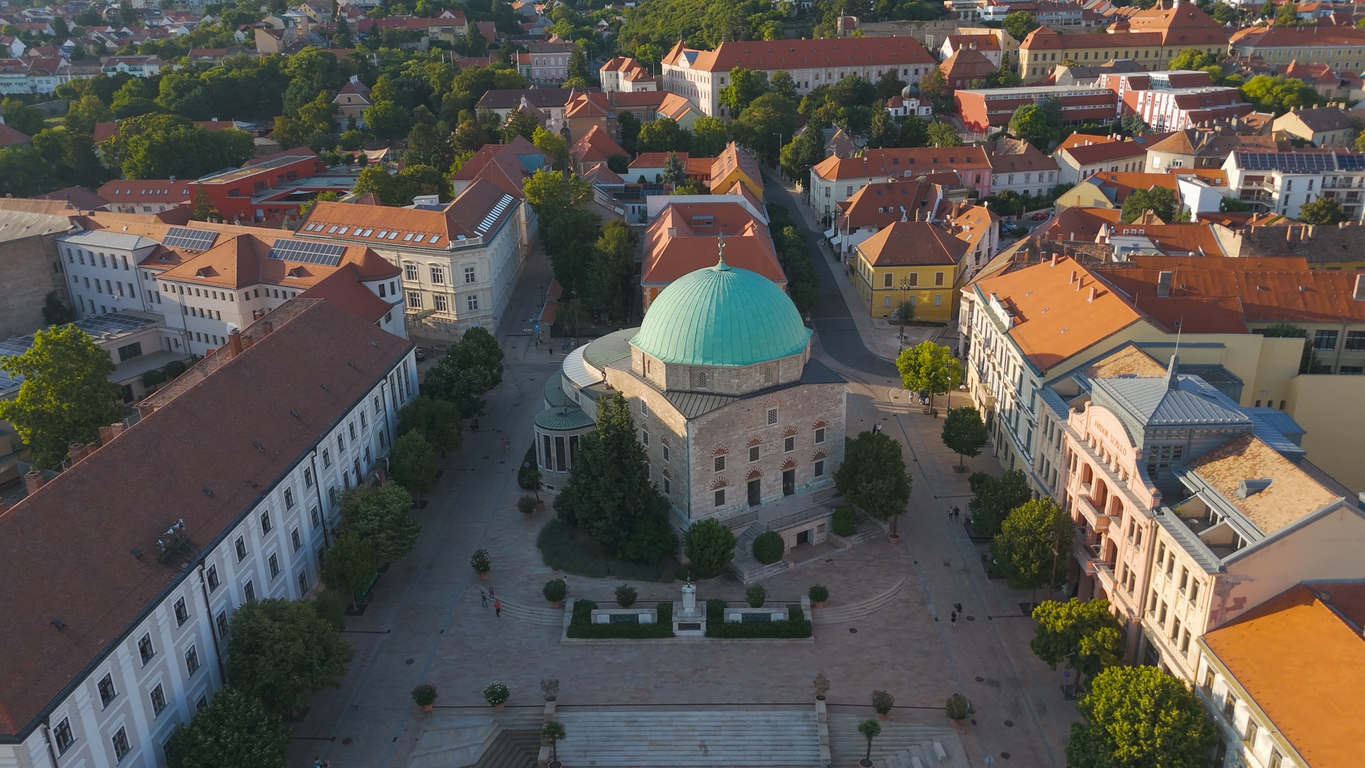 Luftbild des zentralen Platzes in Pécs mit grün bekuppelter Moschee und roten Ziegeldächern.