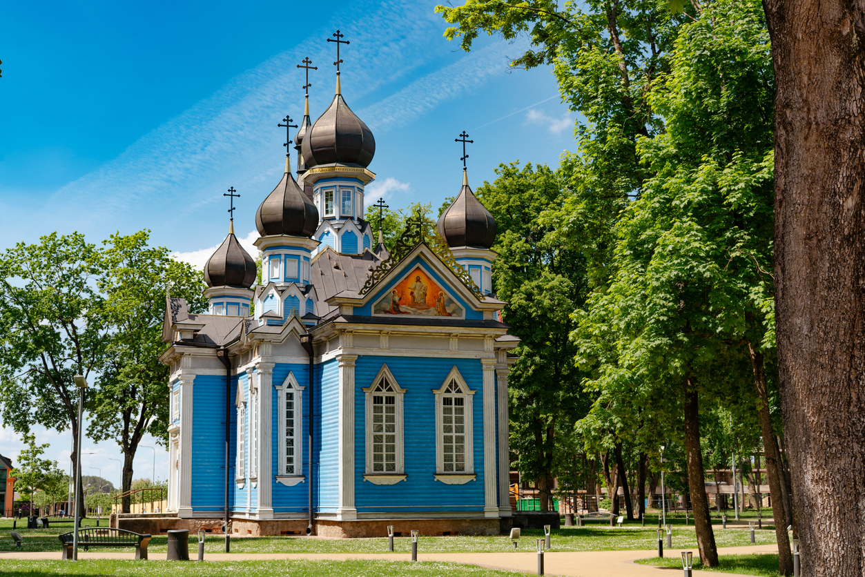 Orthodoxe Holzkirche mit dunklen Zwiebeltürmen in einem grünen Park.
