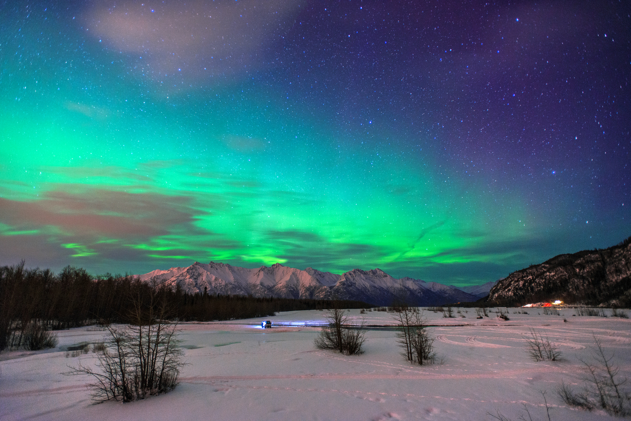 Grünes Aurora-Band leuchtet über verschneiter Landschaft am Knik River in Alaska.