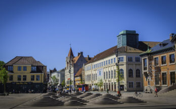 Historische Fassaden, Cafés und eine runde Stufen-Skulptur füllen den Stadtplatz.