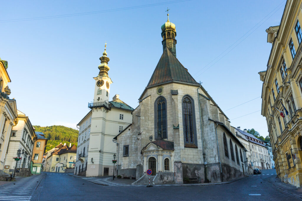 Historische Kirche mit achteckigem Turm neben einem Uhrturm an einer steilen Gasse.