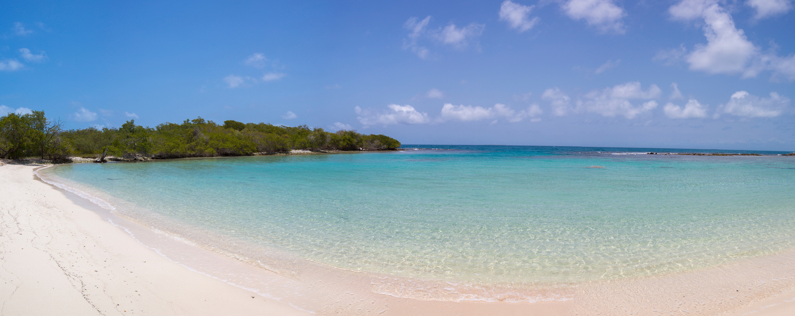 Weißer Sandstrand mit flachem, türkisblauem Wasser und grünen Mangroven im Hintergrund.