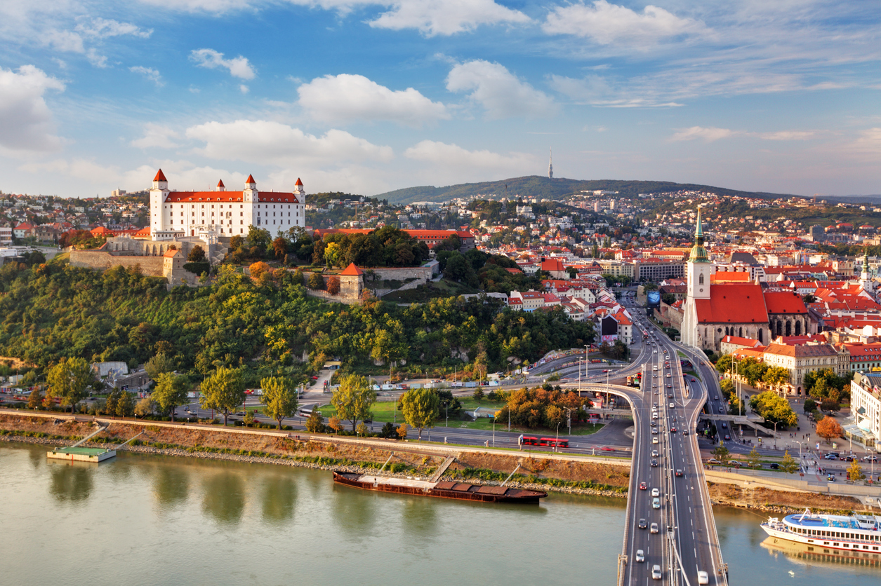 Panorama von Bratislava mit der weißen Burg, dem St.-Martins-Dom und einer Straßenbrücke über die Donau.