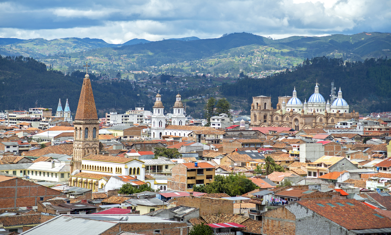 Blick über die roten Dächer von Cuenca mit mehreren Kirchtürmen und Bergen im Hintergrund.