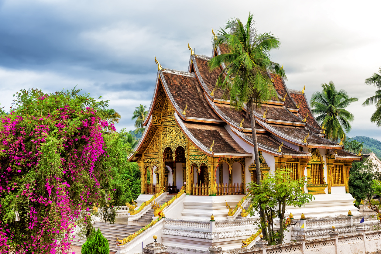 Reich verzierter Tempel in Luang Prabang mit mehrstufigem Dach, Palmen und Treppen.