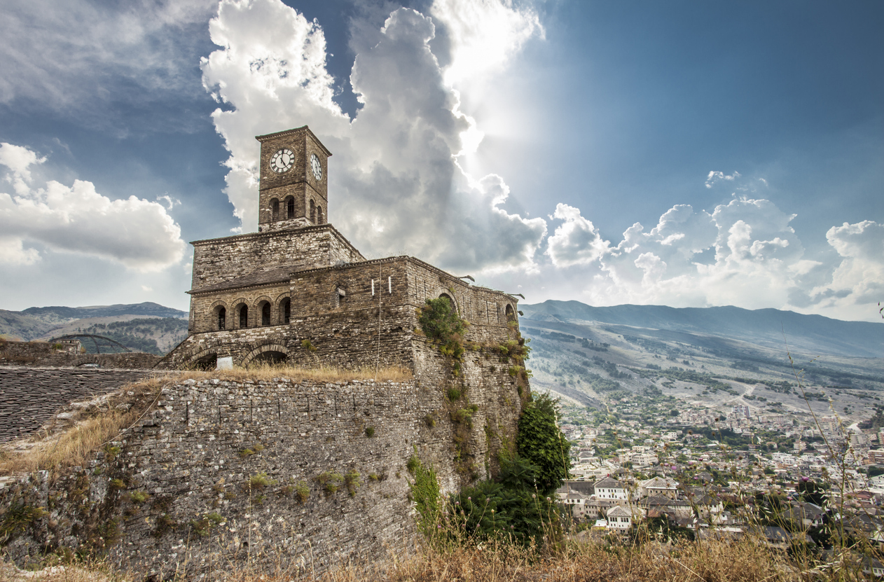 Uhrturm der Burg Gjirokastër über der Stadt mit Bergen und dramatischen Wolken.